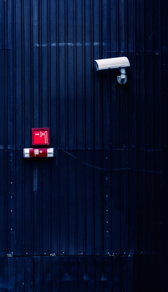 Modern security camera and exit sign on a corrugated metal wall, emphasizing surveillance and safety.